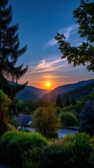 Scenic mountain landscape with setting sun over lush green forests, hills, valley, trees, residential building, and a clear blue sky
