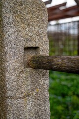 Close-up of a weathered wooden beam inserted into a rough-textured stone pillar. Architectural...
