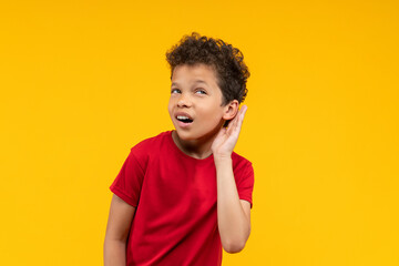 Adorable African American schoolboy posing over bright colored yellow studio background holding...
