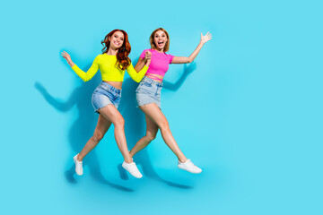 Young fashionable friends leaping with joy in vibrant summer outfits against a teal background, embodying friendship and youthfulness.