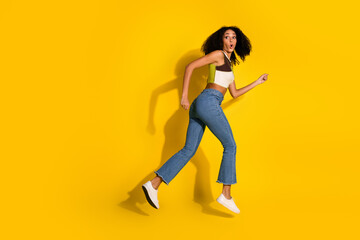 Fototapeta premium Stylish young woman in casual outfit jumping against a yellow background, expressing joy and surprise