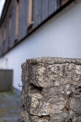 Rough, gray stone pillar with visible layers and texture. Blurred background with a white surface and dark element above.