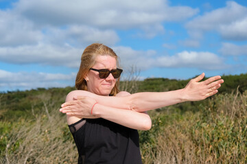 Woman stretching arms outdoors under sunny sky, enjoying fitness and wellness routine in nature, focusing on flexibility, strength, and healthy active lifestyle in fresh air