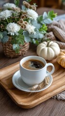 Coffee cup on wooden tray with flowers and small pumpkins in the background on wooden surface with blanket