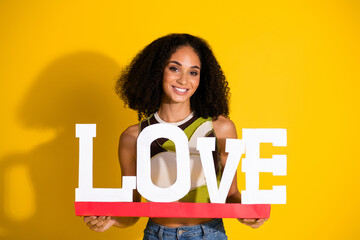 Stylish young woman holding 'love' sign against yellow background, expressing joy and positivity