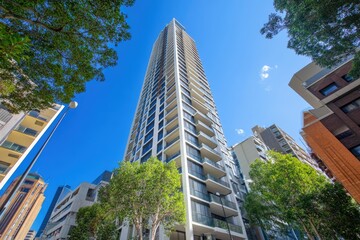 Modern high-rise residential building, viewed from below, showcasing its sleek architecture and numerous balconies.