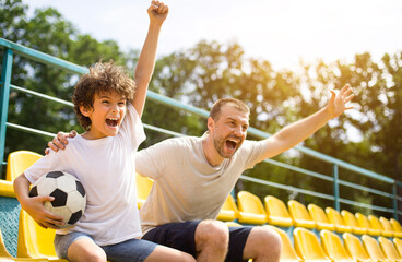 Obraz premium Goal. Emotional man and little boy cheering their favorite team, little boy holding soccer ball