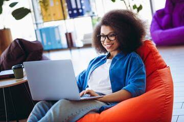 Charming professional woman working on a laptop in a modern office environment with a casual and...