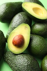 Whole and cut avocados on green background, above view