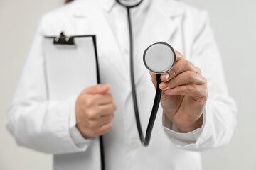 Doctor with stethoscope and clipboard on light background, closeup