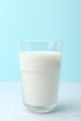 Glass of fresh milk on white tiled table against light blue background