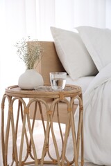 Bedside table with flowers in vase, glass of water and glasses near bed indoors