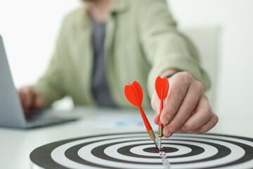 Man with dart aiming at dartboard while working indoors, closeup