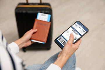 Tourist holding mobile phone with e-ticket for airplane and passport indoors, closeup