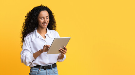Young Brunette Woman Using Digital Tablet, Browsing Internet Or Social Networks, Standing Over Yellow Studio Background, Enjoying Modern Technologies, Checking New App Or Website, Copy Space