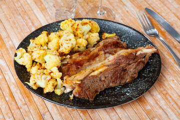 Appetizing and hearty lunch is prepared on plate - several thin slices of roast lamb, garnished with stewed cauliflower.