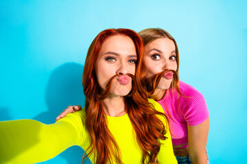 Playful young girlfriends having fun with hairstyles against a vibrant turquoise background