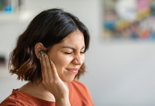 Sick young arab woman having ear pain at home, upset middle eastern female rubbing sore auricle with hand and frowning, suffering from otitis and acute ache, closeup shot with copy space