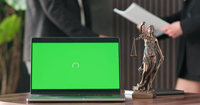 A laptop with a green screen and a statue of justice in the background of business people. The concept of legal support and justice.