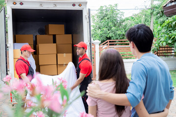 Happy Asian couples using professional moving house services standing in front of new house receive...