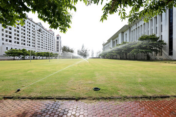 Closeup of Sprinkler Splash Water over grass field to water in the grass among the buildings at Thailand.