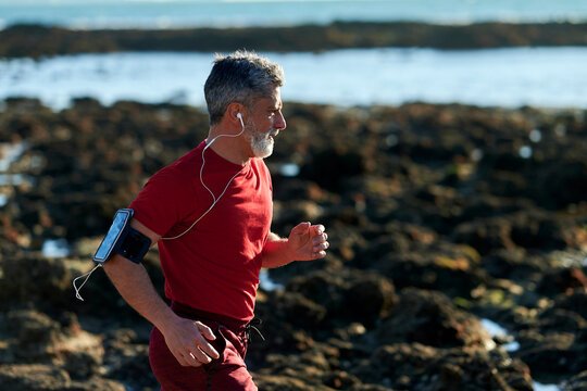 Senior man jogging by the sea while listening to music - Powered by Adobe