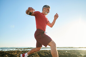 Senior man running on the beach wearing sport clothes and earphones