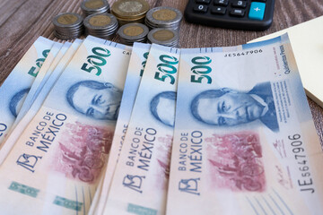 500 Mexican peso bills with coins on one side, nearby is a calculator