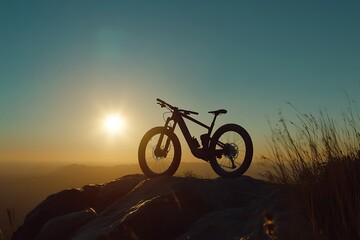 Obraz premium Silhouette of a mountain bike sits atop a rock formation at sunset
