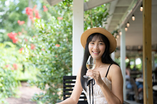 Elegant Asian Woman Savoring White Wine at a Scenic Winery.