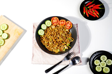 Top view of Tektek Fried Noodles or Mie Tektek, Indonesian spicy savory traditional noodle, served with sliced cucumber, sliced tomato and other vegetables
