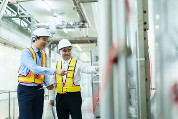 Asian engineer and manager inspect steam pipes and boiler system in a food manufacturing factory.