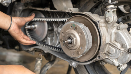 Mechanic adjusting scooter CVT belt system during repair. Visible clutch, variator, and drive belt inside the open transmission case. Hands-on maintenance and tuning process.