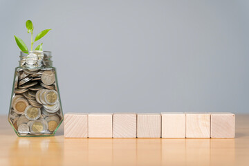 Savings and investment concept. Seven wooden blocks. Young plant growing in the glass jars that have money.