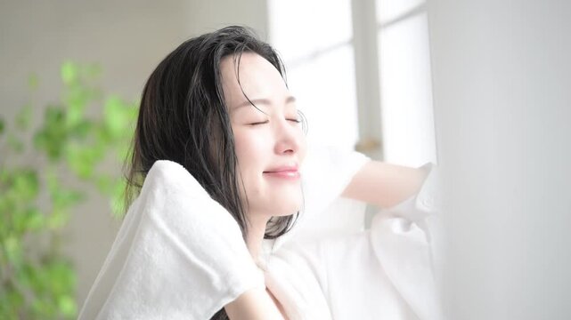 逆光の窓辺で朝やお風呂上りなどに濡れた髪を乾かすタオルドライする笑顔の女性の横顔の動画