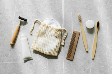Hygiene products as bamboo toothbrushes, toothpaste, reusable pads, safety razor on grey marble...