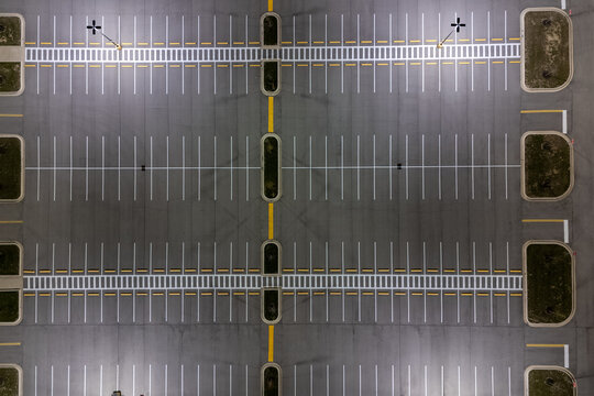 Overhead view of empty parking lot with rows of white lines under a bright sunny sky.