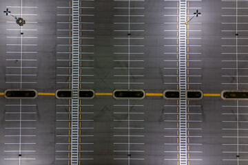 Overhead view of empty parking lot with rows of white lines under a bright sunny sky.