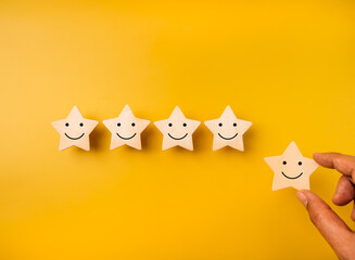 Happy smile face emoticon on stars, on yellow background and hand holding one star for more rating satisfaction. Customer evaluation, 5 rates excellence quality service, business marketing concept.