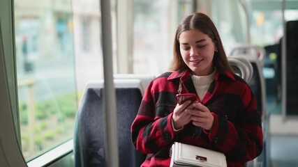 During trip to work in tram car, passenger girl with phone sitting and scroll through social media feed, red news. Girl in urban electric vehicle gets to terminal station - Powered by Adobe