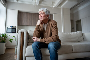 Sad sorrowful senior man sit in quiet contemplation supporting head with hand, looking through...