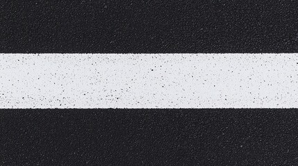 Fototapeta premium A white road line on black asphalt, viewed from above, showing a simple, textured street marking.