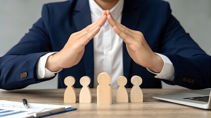 A businessman in a suit forming a roof with his hands over wooden figures, illustrating concepts of protection, teamwork and leadership in corporate culture.
