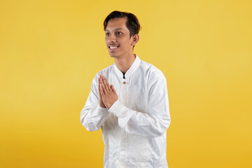 Smiling muslim man wear white shirts with Islamic ornaments while gesturing a greeting with his...