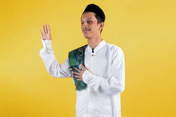Smiling muslim man wear white shirts with Islamic ornaments and a prayer mat waving goodbye in a...