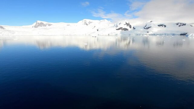 Sailing slowly into Neko Harbour Andvord Bay Antarctic Peninsula mountain reflected in calm blue water