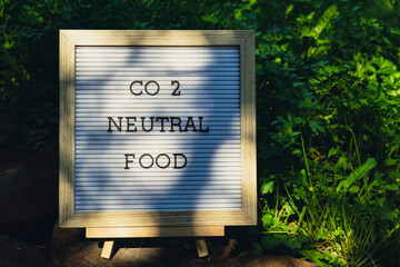 Letter board with text CO2 NEUTRAL FOOD on background of garden bed with green herb parsley. Organic farming, produce local vegetables concept. Supporting local farmers. Seasonal market 
