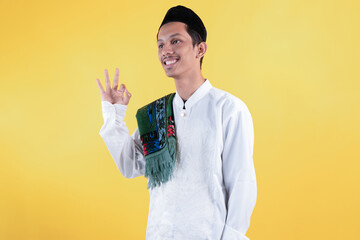 Smiling muslim man wear white shirts with Islamic ornaments and a prayer mat on the shoulder with...