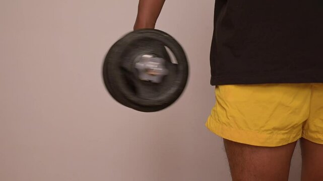 Unknown male doing wrist rotation exercise with dumbbell or pronation and supination of forearm with dumbbell indoors.