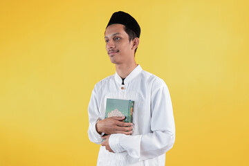 Smiling muslim man wear white shirts with Islamic ornaments while holding Holy book of Quran